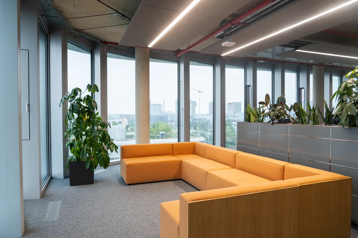Lounge mit orangefarbenem Sofa und Fensterfront in der 7. Etage